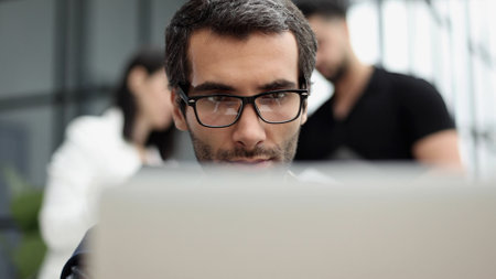 Portrait of handsome bearded man wearing glasses working with laptop in office late, his face lit up by screenの写真素材