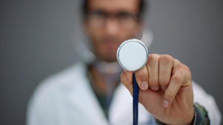 Close-up portrait of doctor showing stethoscope on gray backgroundの写真素材