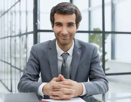 I call the shots around here. Shot of a handsome young businessman sitting on his desk in the office with his arms folded.の写真素材