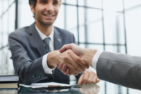 Portrait of confident mature specialist sitting at the table and reaching out his hand to the camera for a handshakeの写真素材