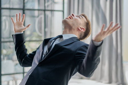 A joyful businessman standing with hands raised in victory and looking upの写真素材