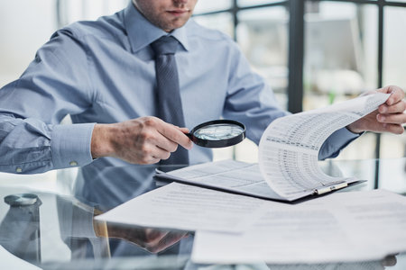 Businessman looking through a magnifying glass to documentsの写真素材