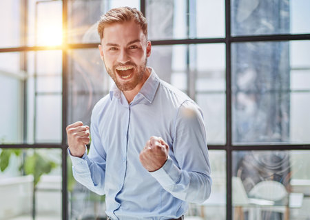 Portrait of a young businessman in a blue shirt shaking his fists celebrating his successの写真素材