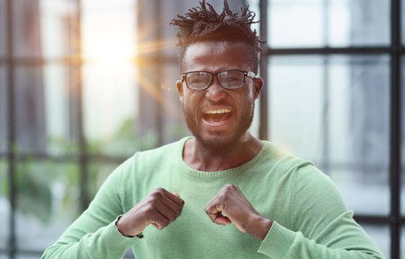 human emotions, reactions and feelings. Joyful young black man in glasses clenching his fists expressing joy and success,の写真素材