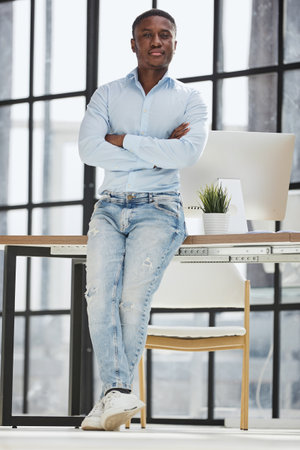 african american man sitting on desk and posing with folded handsの写真素材