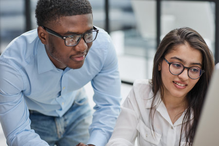 Cheerful multiracial colleagues discussing startup project and smiling during workday in office interiorの写真素材