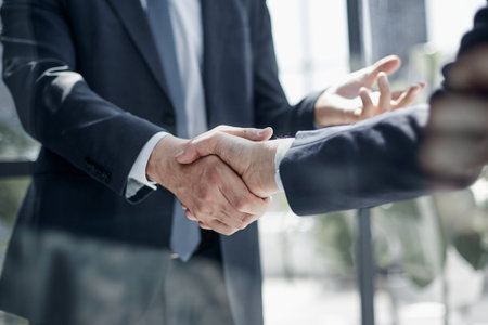 executives shaking hands in front of their manager and a colleagueの写真素材