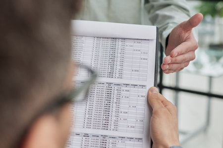 male accounting manager reviewing financial report, sitting at table alone at officeの写真素材