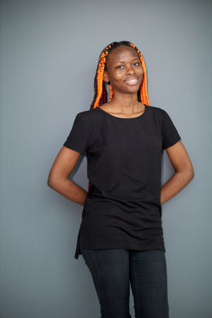 a black woman on a gray background stands holding her hands behind her back