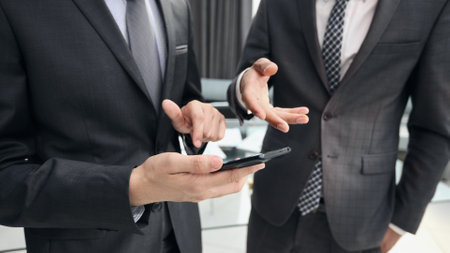 two businessmen using smartphone stands in office corridorの写真素材