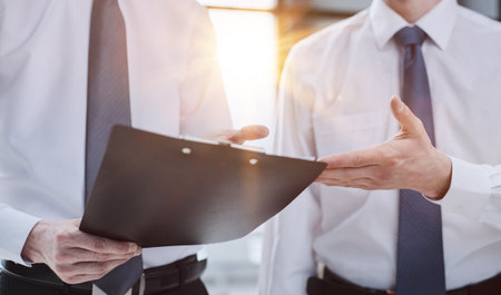 Businesspeople in suits holding a black document folder and pondering about future career opportunities.の写真素材