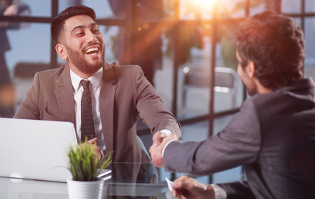 two confident business men shaking hands at the office tableの写真素材
