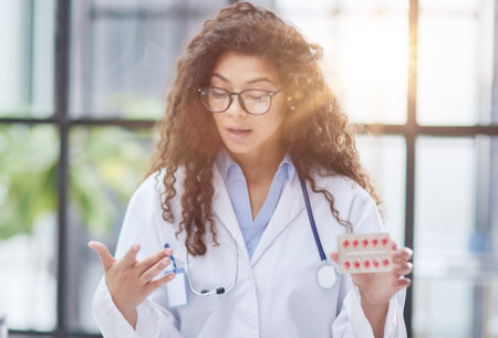 Young pharmacist woman holding pills while sitting at the table in the officeの写真素材