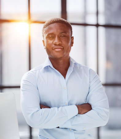 african american man sitting on desk and posing with folded handsの写真素材
