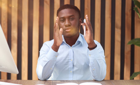 African american businessman holding pen and sitting at office deskの写真素材