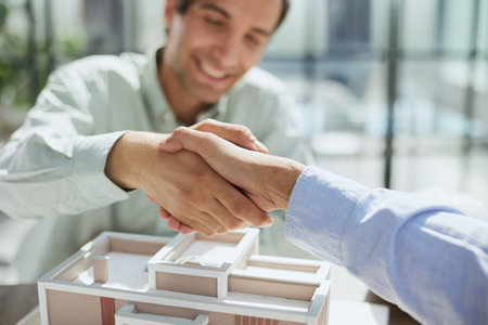 handshake against the background of a model of a house under construction. client and designerの写真素材