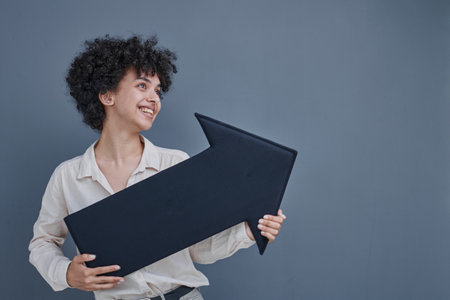a girl on a gray background smiles, holds a black arrow in her hands, points to the side