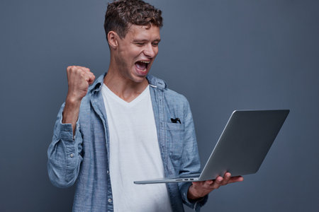 young man on a gray background holding a laptopの写真素材