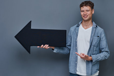 a young man on a gray background holds a black arrow in crayfish. shows directionの写真素材