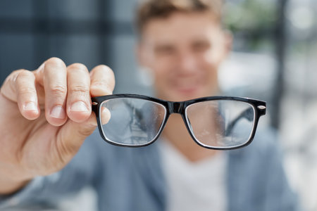 a young man in a bright office looks at you through his glassesの写真素材