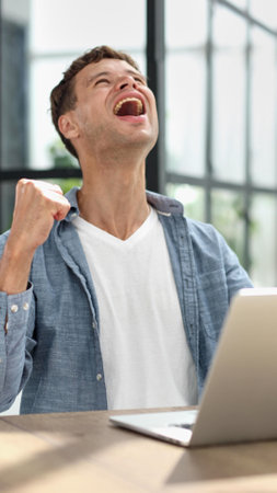 Businessman in the office joyfully raises his hands up celebrating victory and success in his work