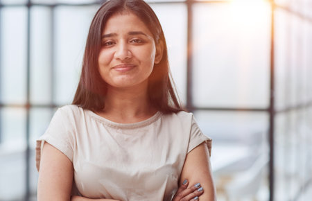 portrait of a smiling business woman with her arms crossed against the backdrop of the officeの写真素材
