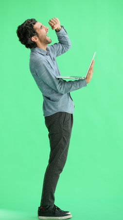 young man in full growth. isolated on green background using laptopの写真素材