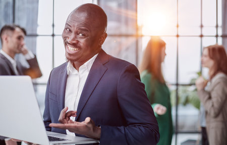Young african american man in business suit holding laptop while standing at office corridorの写真素材