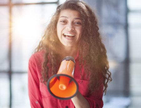 Beautiful girl shouting into a megaphone in a modern officeの写真素材