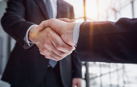 executives shaking hands in front of their manager and a colleagueの写真素材