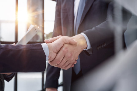 executives shaking hands in front of their manager and a colleagueの写真素材