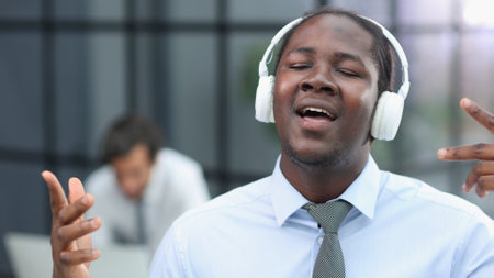 a man at a workplace at a table in front of a computer with headphones listening to musicの写真素材