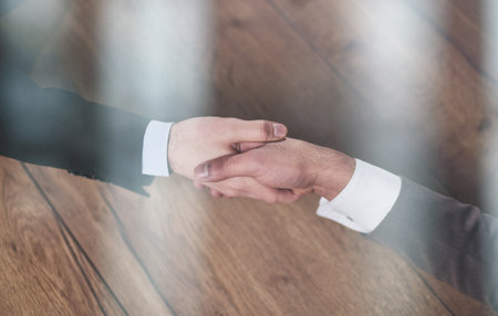 Closeup of hands of two young and successful male business people shaking hands over wooden tableの写真素材