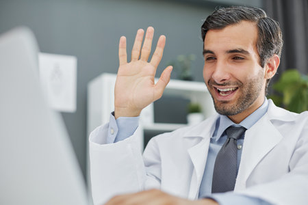 doctor waving hand to patient via laptop video linkの写真素材