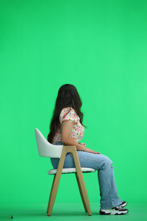 A woman, on a green background, full-length, sitting on a chair, in profile