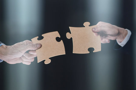 Close-up of business partners putting together white puzzle pieces on black background