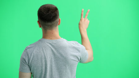 A man in a gray T-shirt, on a green background, close-up, shows a victory signの写真素材