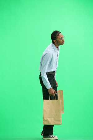 A man in a gray shirt, on a green background, full-length, with bags