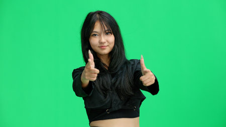 A girl in black clothes, on a green background, points forwardの写真素材