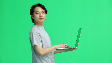 A guy in a gray T-shirt, on a green background, close-up, with a laptop