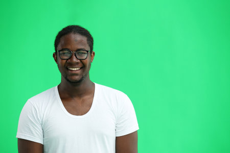 A man in a white T-shirt on a green background close-up points his fingers to the side