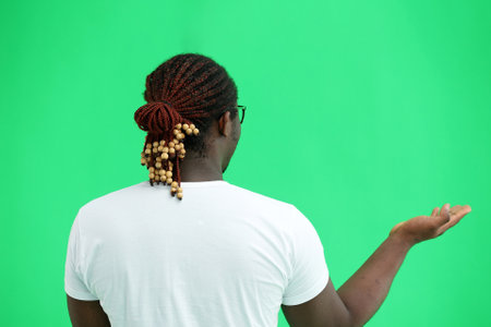 A man in a white T-shirt on a green background close-up points his fingers to the side, back view