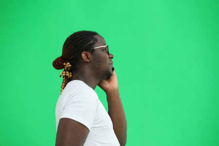 A man in a white T-shirt on a green background talks on the phone, in profileの写真素材
