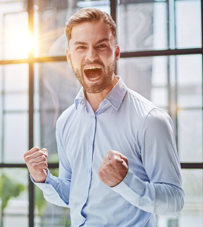 Portrait of a young businessman in a blue shirt shaking his fists celebrating his successの写真素材