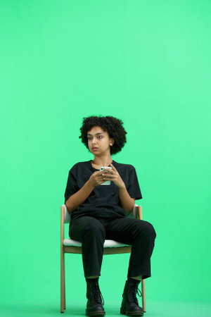 A woman, full-length, on a green background, sitting on a chairの写真素材