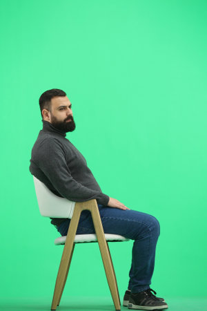 A man, full-length, on a green background, sitting on a chairの写真素材