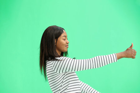 A woman, on a green background, in close-up, shows her thumbs up