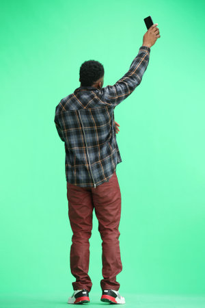 A man, full-length, on a green background, waving his phoneの写真素材