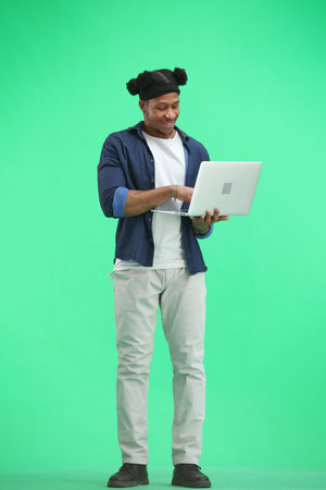 A man, full-length, on a green background, uses a laptop