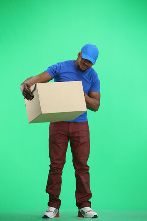 The deliveryman, in full height, on a green background, looks at the box